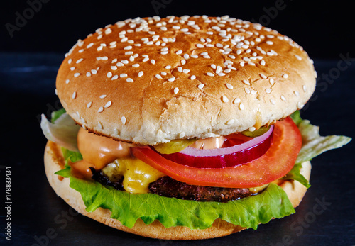 Hamburger with beef, cheese, onion, fresh salad and soft buns with sesame seeds on a dark background of natural stone. photo