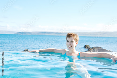 Young cheerful girl swimming in water of pool looking away on background of sea, Iceland, West Fjords. © vitaliymateha