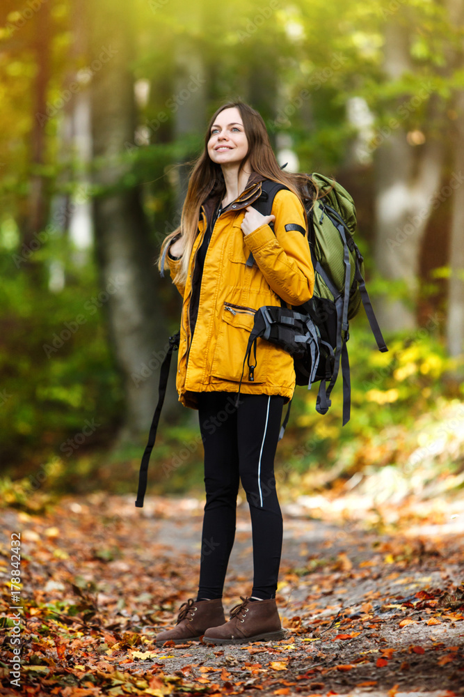 Cheerful brunette tourist girl wears orange jacket and backpacked have walk through forest, autumn tourism concept Cheerful brunette tourist girl wears orange jacket and backpacked have walk through forest, autumn tourism concept