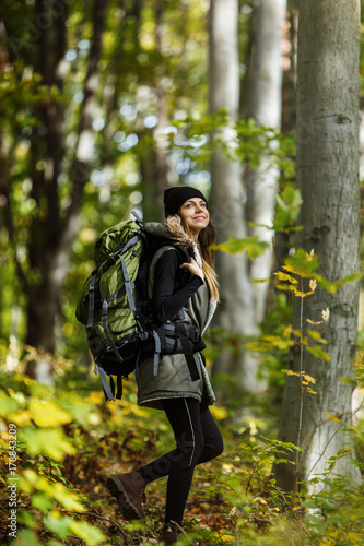 Cheerful brunette tourist girl wears black cap and backpacked have walk through forest, autumn tourism concept