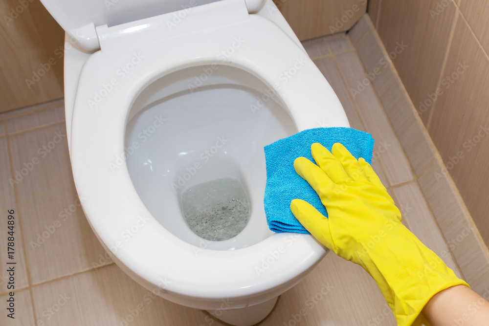 A hand in a yellow glove washing a toilet bowl A hand in a yellow glove washing a toilet bowl