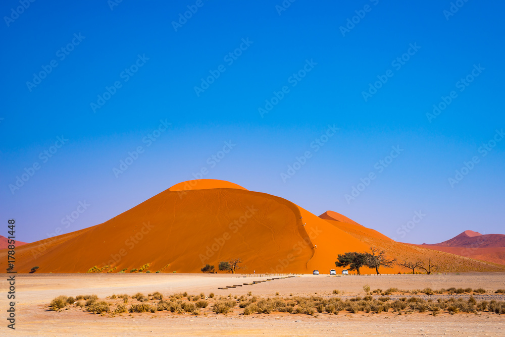 Tourists climbing sand dune at Sossusvlei, Namib desert, Namib Naukluft National Park, Namibia. Traveling people, adventure and vacations in Africa.