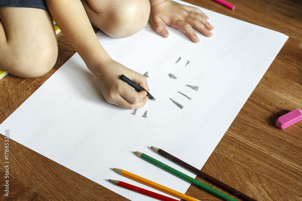 Girl draws picture with crayons on the sheet of paper on the floor Girl draws picture with crayons on the sheet of paper on the floor