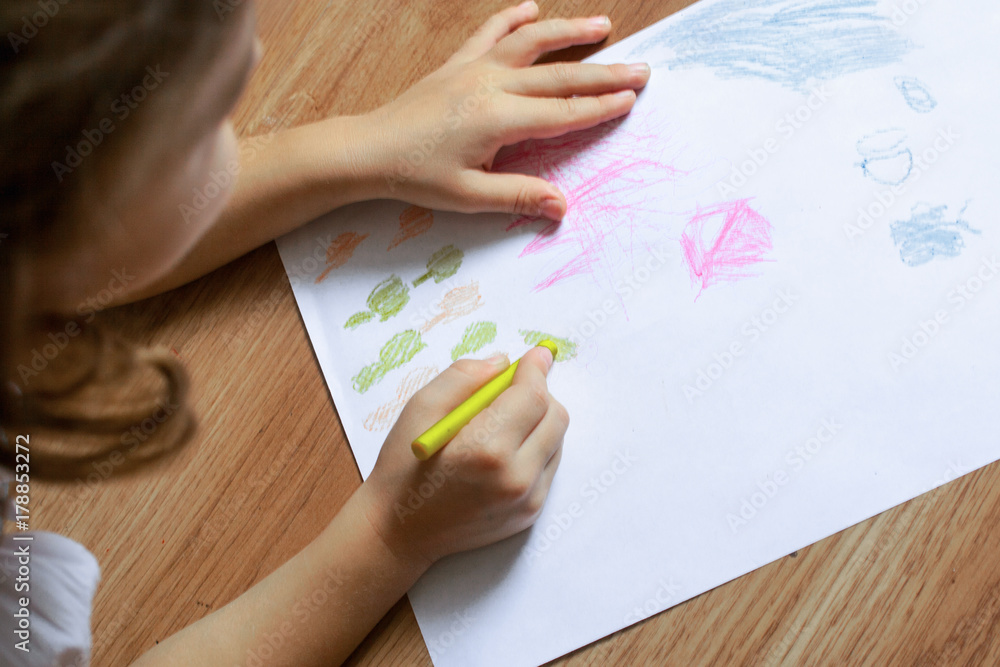 Girl draws picture with crayons on the sheet of paper on the floor Girl draws picture with crayons on the sheet of paper on the floor