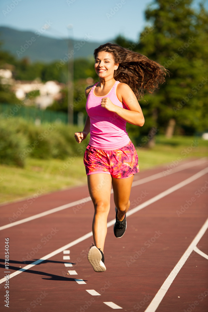 active young woman runs on atheltic track on summer afternoon active young woman runs on atheltic track on summer afternoon