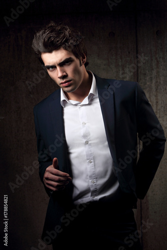 Sexy handsome male model posing in blue fashion suit and white style shirt on dark shadow background