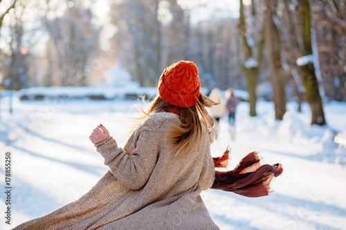 Young gorgeous lady  in a warm hat and scarf walking  with thermocup in hands on the background of the  winter park. photo