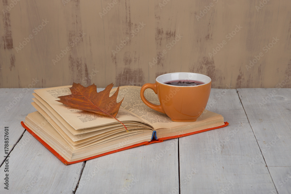 Concept of autumn resting - cup of tea with autumn colorful leaves and book on white wooden table and brown background Concept of autumn resting - cup of tea with autumn colorful leaves and book on white wooden table and brown background