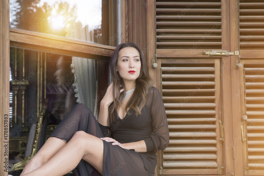 wooden window and beautiful woman. Portrait of fashion serious beautiful woman is wearing black dress near wooden wall with window wooden window and beautiful woman. Portrait of fashion serious beautiful woman is wearing black dress near wooden wall with window