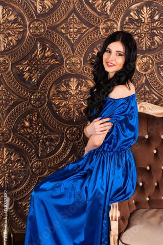 young woman in elegant blue gray evening dress indoors with beautiful interior