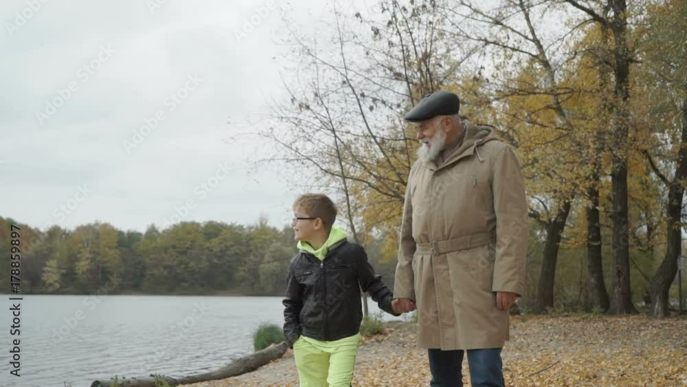 Grandfather walks in autumn park near the river with little grandson Grandfather walks in autumn park near the river with little grandson