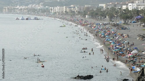 Landscape of mediterranean beach with crowd of people bathing in summer at sunset photo