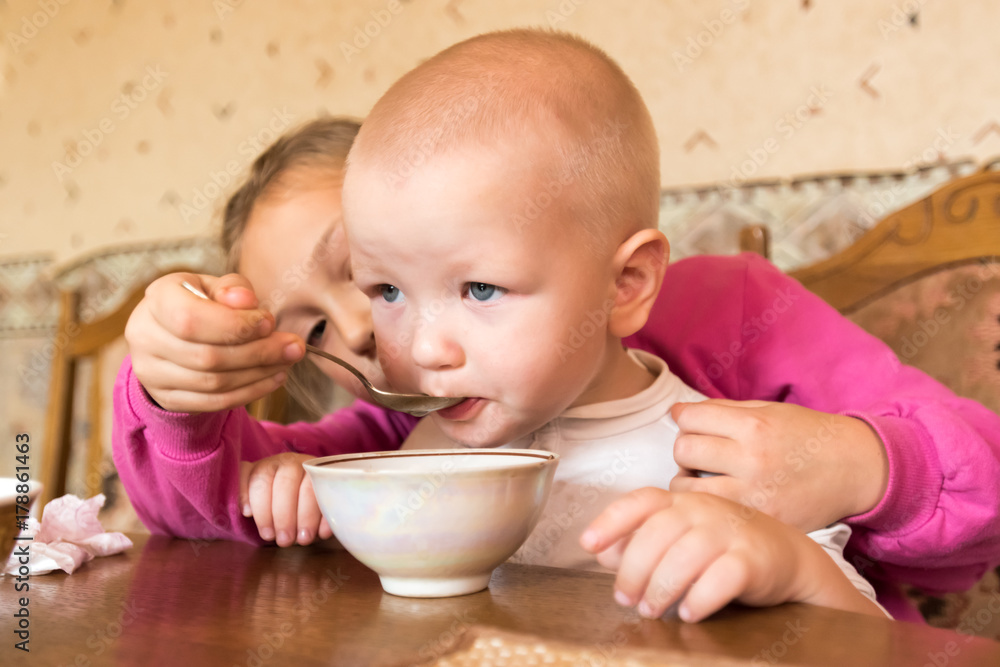 The elder sister takes care of a little brother and treats with tea and rolls. Selective focus. The elder sister takes care of a little brother and treats with tea and rolls. Selective focus.