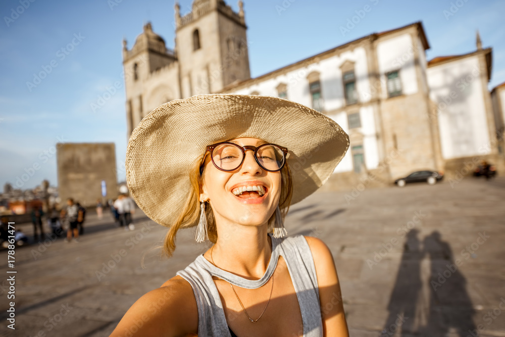 Young woman tourist making selfie photo with phone standing in front of the main cathedral in Porto city during the sunset in Portugal