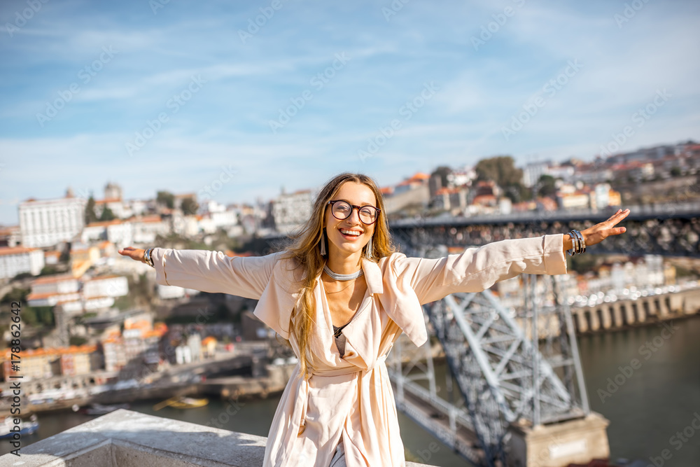 Portrait of a young woman tourist with raised hands sitting on the beautiful cityscape background with famous bridge in Porto city, Portugal