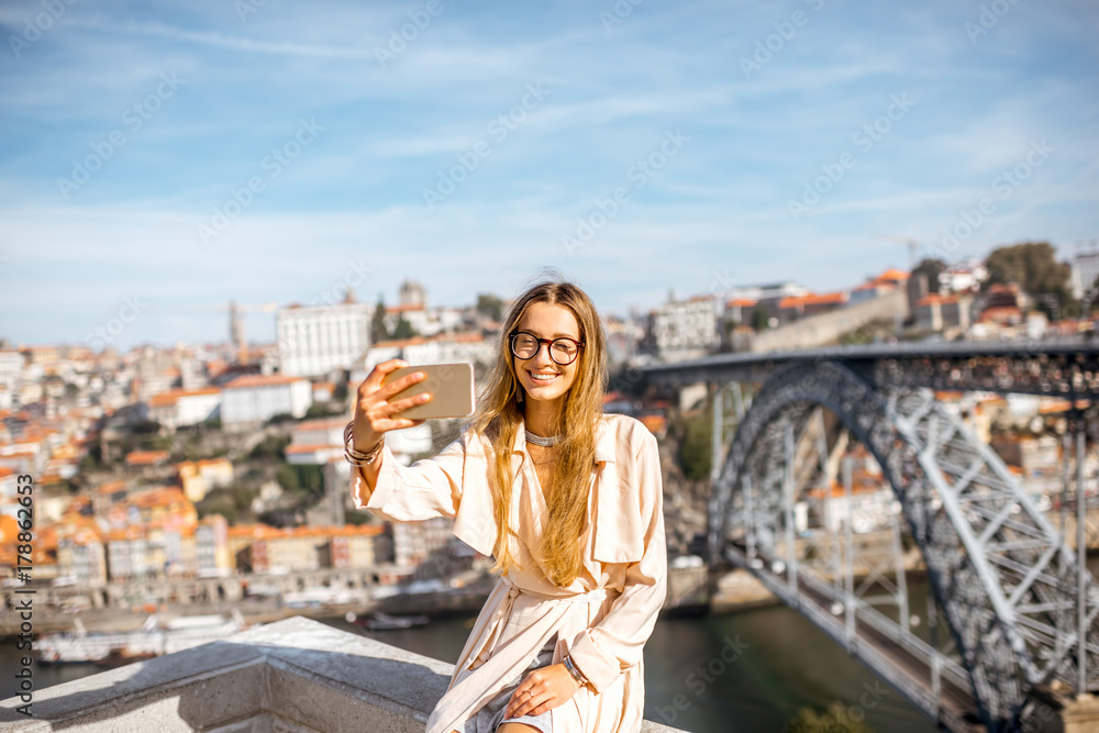 Young woman making selfie photo with phone on the beautiful cityscape background with famous bridge in Porto city, Portugal