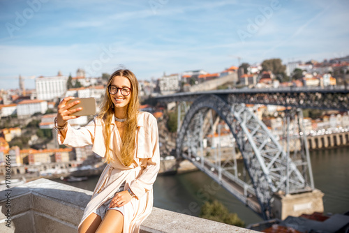 Young woman making selfie photo with phone on the beautiful cityscape background with famous bridge in Porto city, Portugal © rh2010