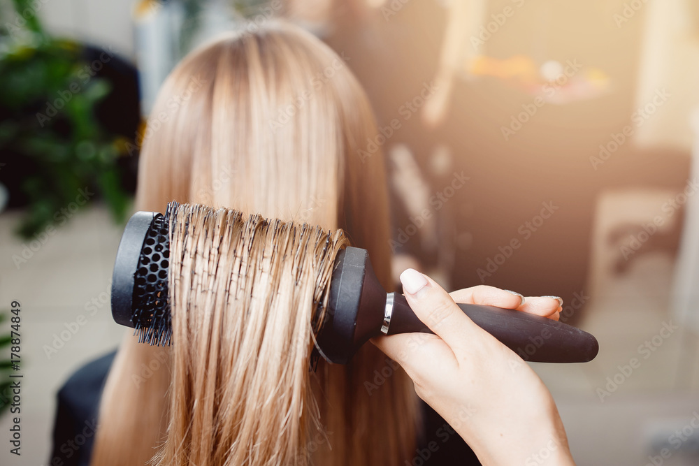 Fototapeta premium Stylist puts a hair dryer and comb hair in a hairdresser