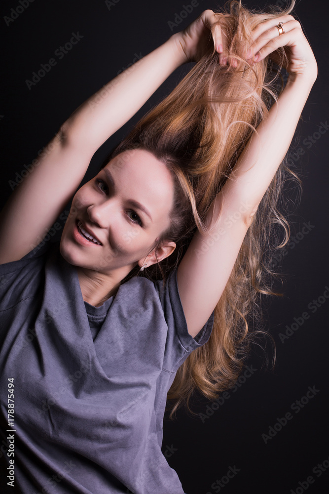 Pretty young model pulling her hair, wears grey shirt,  posing on a black background