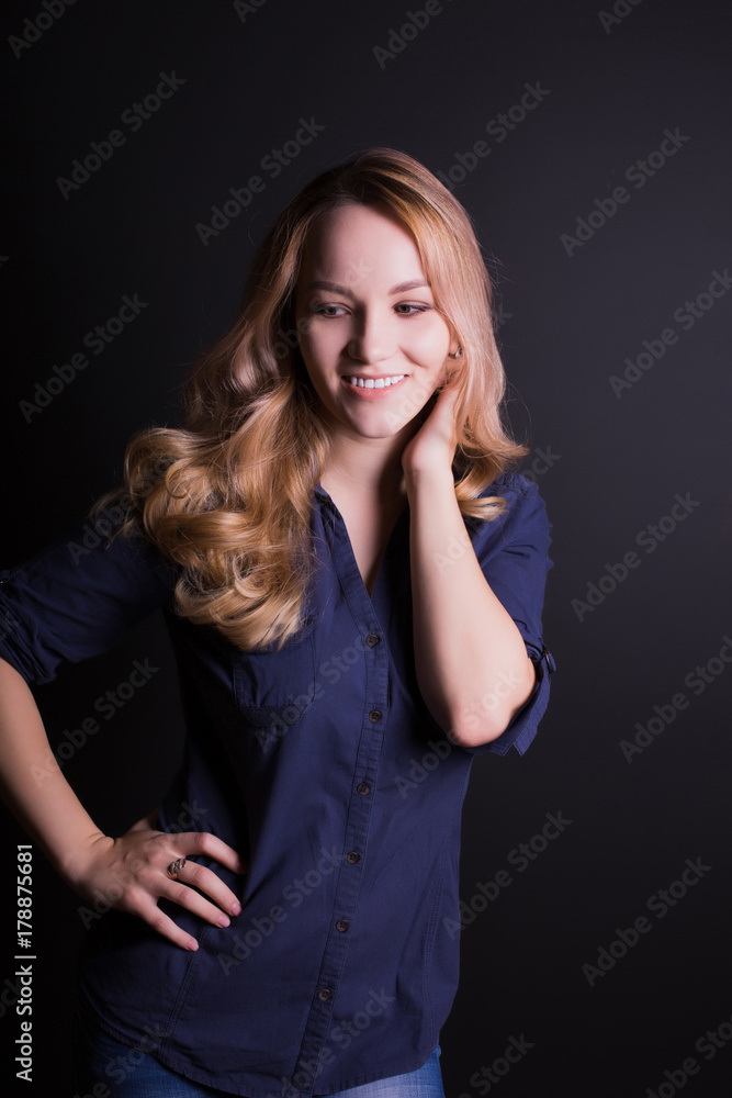 Romantic young model with long blonde hair wears shirt and jeans, posing on a black background Romantic young model with long blonde hair wears shirt and jeans, posing on a black background