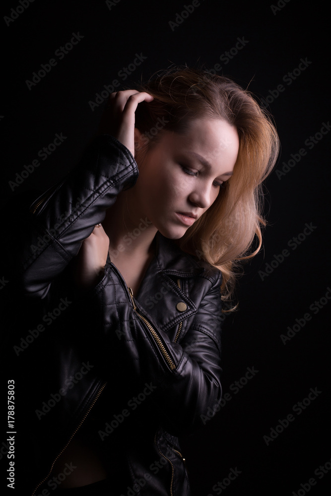 Sensual young model with lush wavy hair, wears leather jacket, posing with shadow on her face Sensual young model with lush wavy hair, wears leather jacket, posing with shadow on her face