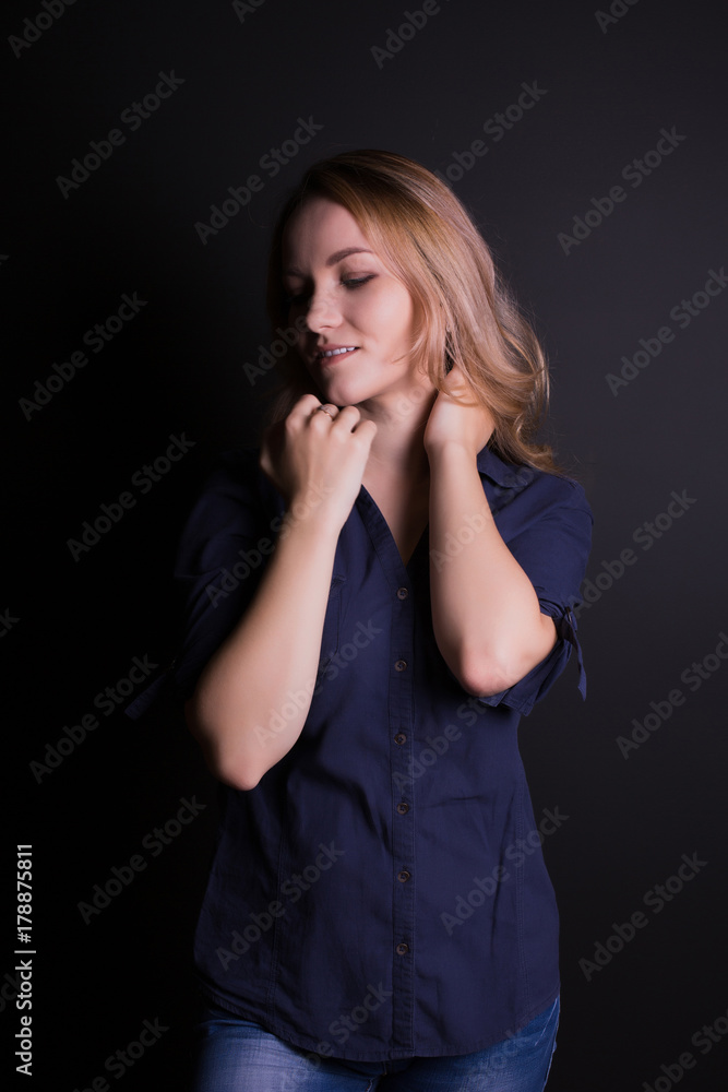 Studio shot of sensual blonde woman wears blue shirt, jeans posing on a black wall Studio shot of sensual blonde woman wears blue shirt, jeans posing on a black wall
