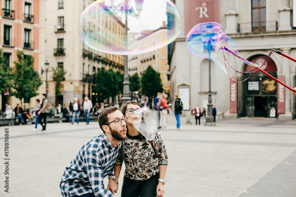 Obraz premium .A young couple in love walking around Madrid and enjoying a very fun day of sightseeing around the city center. Playing with giant soap bubbles. Lifestyle