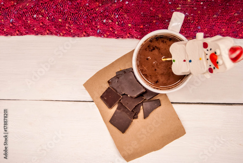 Hot chocolate in a cup with mashmellow in the form of a snowman, pieces of dark chocolate and warm knitted clothes. What will warm in the cold photo