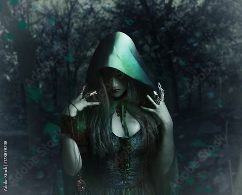 Beautiful sorceress in green cloak holding antique watch standing in the night forest photo.