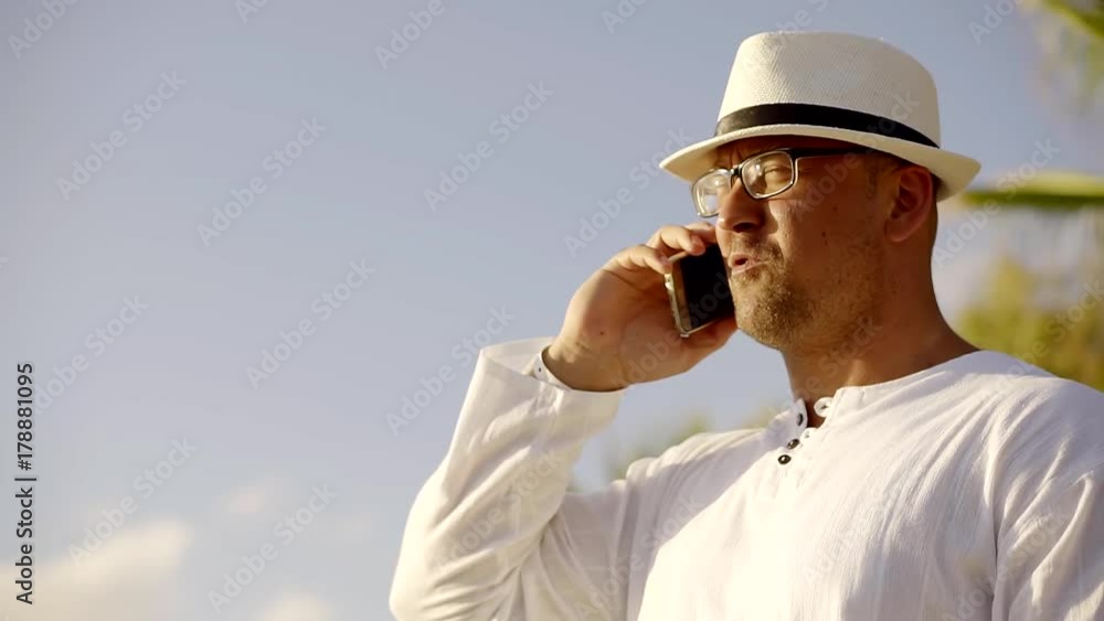 serious adult man is conducting telephone conversations, standing on a summer street during holidays serious adult man is conducting telephone conversations, standing on a summer street during holidays
