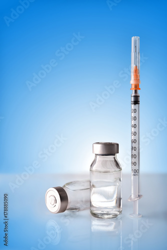 Vials and syringe on white table with blue background vertical