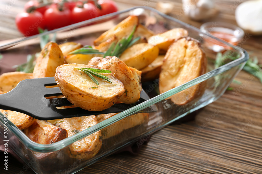 Delicious baked potatoes with rosemary on spatula above baking dish, closeup Delicious baked potatoes with rosemary on spatula above baking dish, closeup