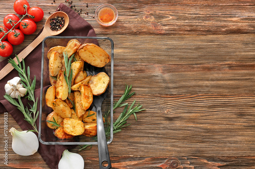 Composition with delicious rosemary potatoes in baking dish on table