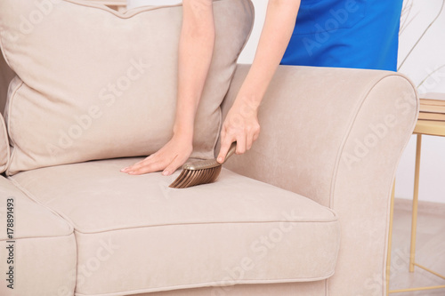 Woman cleaning couch with brush at home