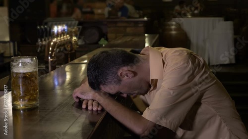 Too drunk guy holding his head on the bar cannot reach his glass