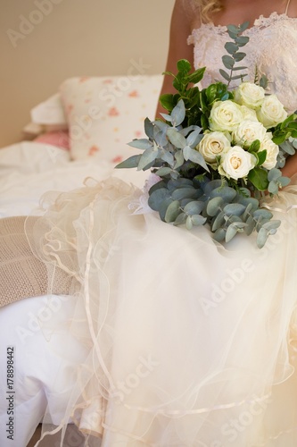 Midsection of bride in wedding dress holding bouquet on bed