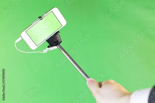 Selfie Stick on a green background. Selfie stick with phone on a green background close-up. From the first person. The phone has a green screen