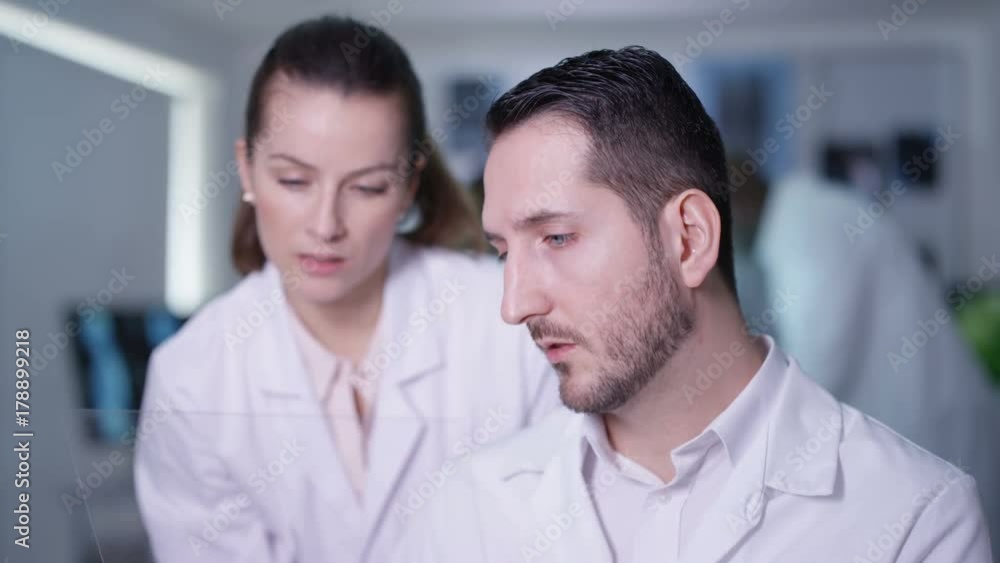 Scientists in lab holding piece of clear material and using as interactive touch screen. Futuristic laboratory, science and research concept.