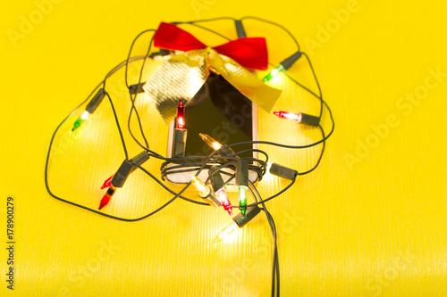 Wallpaper Mural Phone as a gift for the new year. Mobile phone in a garland and bow on a yellow background with a green screen, a gift for Christmas Torontodigital.ca