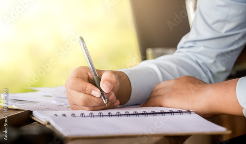 Close up businessman with pen writing on notebook at his home office on wooden desk