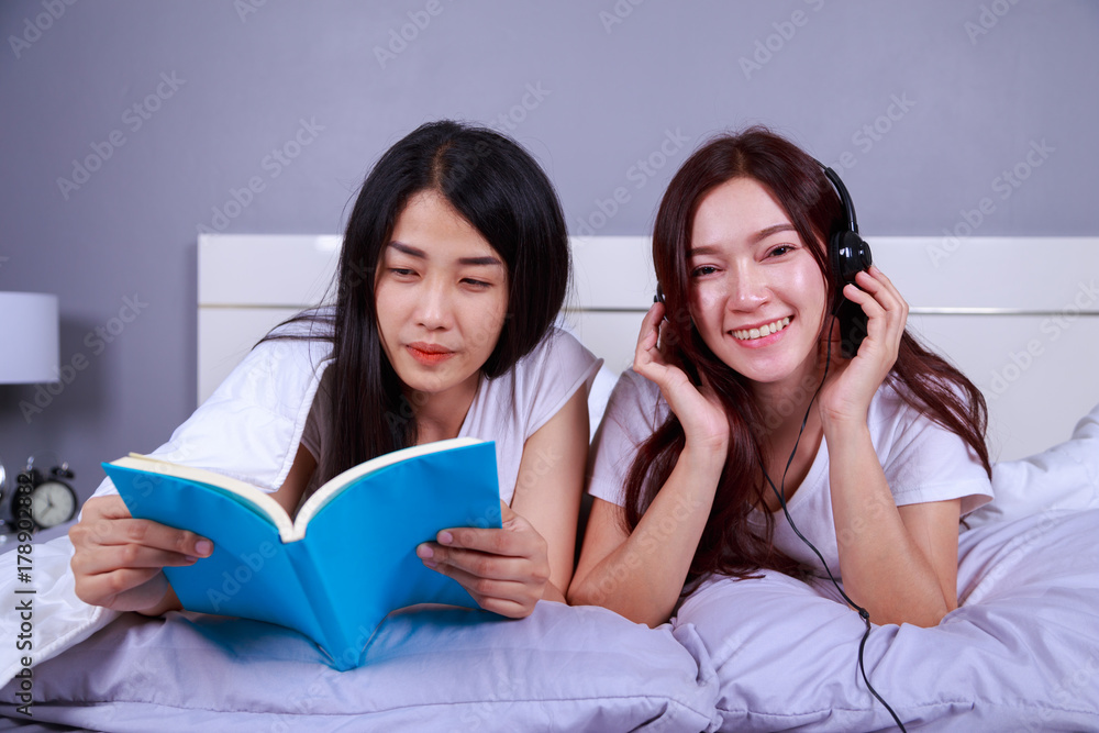two woman reading a book and using smart phone on bed in bedroom two woman reading a book and using smart phone on bed in bedroom