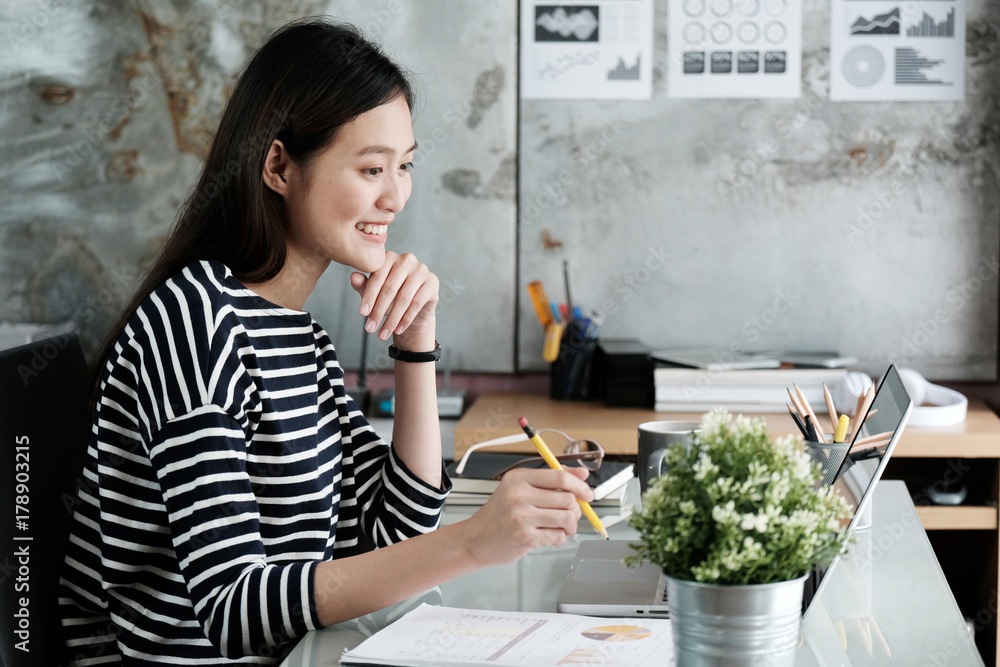 Young asian businesswoman working at office table with smiling face, positive emotion, casual office life concept