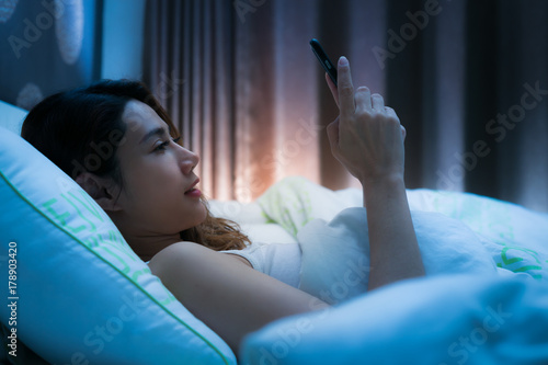 Woman on bed late at night texting using mobile phone tired falling sleep.