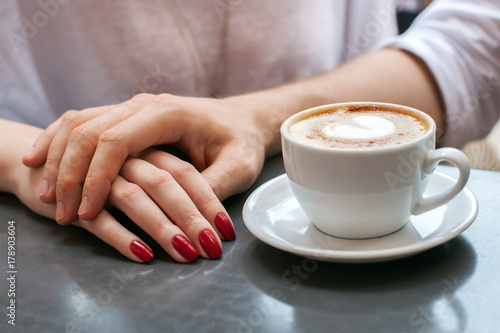 Hands of a man and a woman and coffee cup on a table