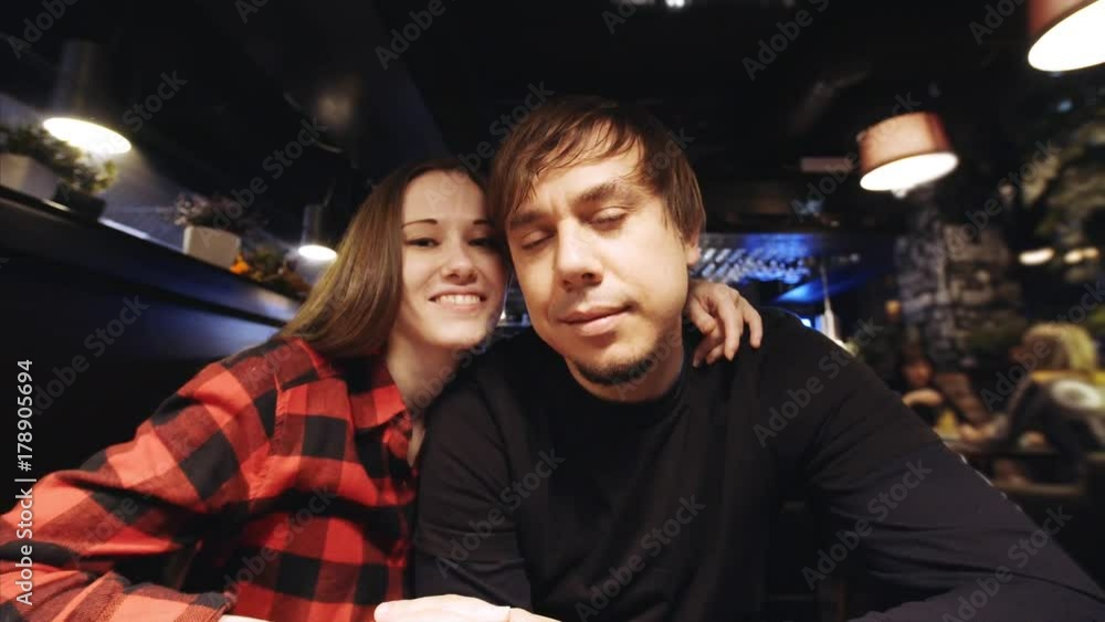 Young couple is looking into the camera and smiling. Pretty woman is giving her boyfriend a loving kiss in a restaurant. Camera is zooming in and out Young couple is looking into the camera and smiling. Pretty woman is giving her boyfriend a loving kiss in a restaurant. Camera is zooming in and out