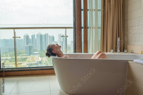 Young woman in white bath in luxury bathroom with city view
