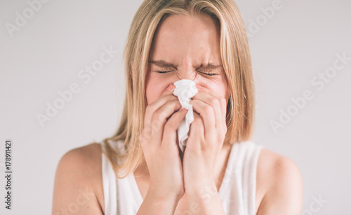 studio picture from a young woman with handkerchief. Sick girl isolated has runny nose. Female model makes a cure for the common cold.