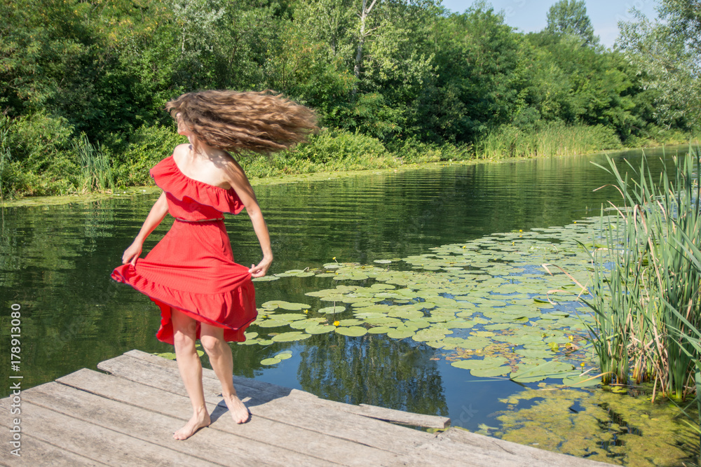 Beautiful young woman in red dress by the river water