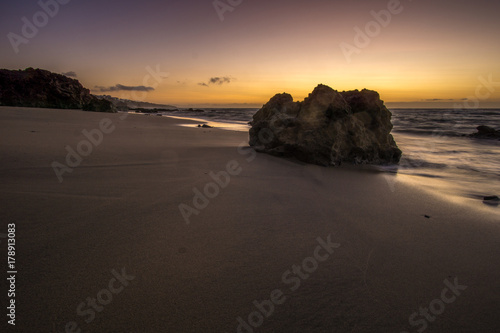 a rock on the beach at sunrise and waves