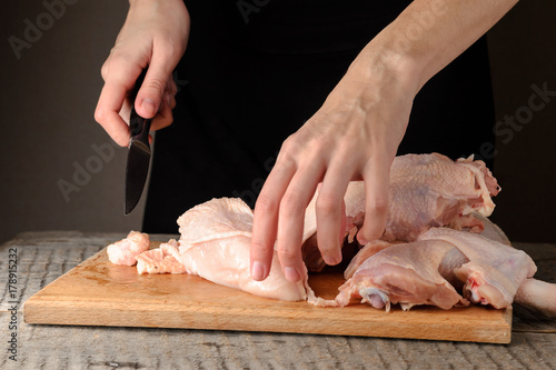 a man knives a raw chicken into pieces on a cutting board.